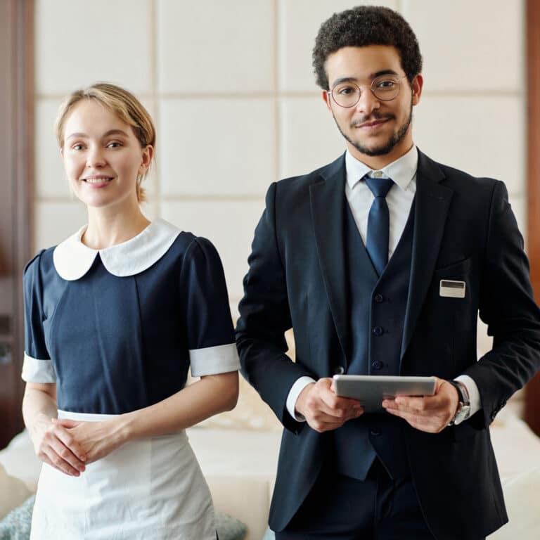 Young successful staff of luxurious five star hotel standing against couch