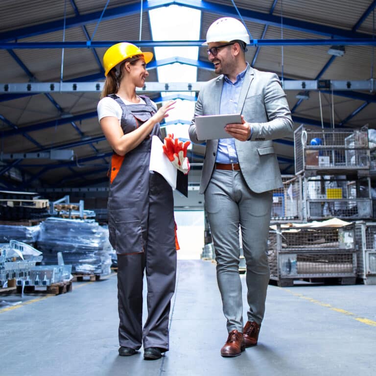Manager supervisor and industrial worker in uniform walking in large metal factory