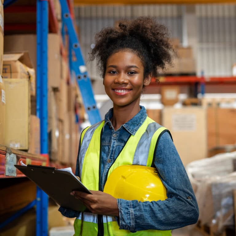 Female staff smiling with holding clipboard standing in warehouse